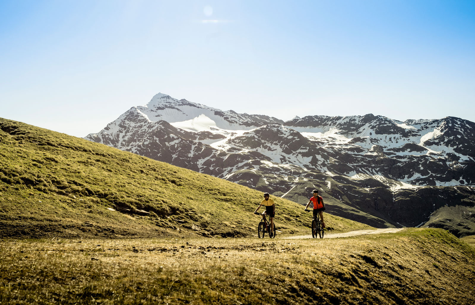 Cyclists on a mountain path with snowy peaks in the background